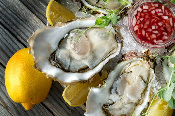 Large fresh oysters with sweet dipping sauce and lemons on a plate of crushed ice.