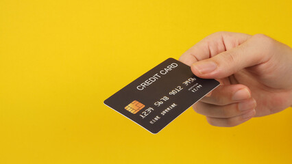 Hand is holding black credit card on yellow background.