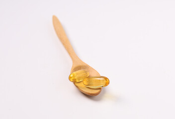 fish oil capsules, wood spoon on white background and supplements concept