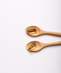fish oil capsules, wood spoon on white background and supplements concept