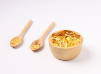 fish oil capsules, wood spoon and wood cup on white background and supplements concept