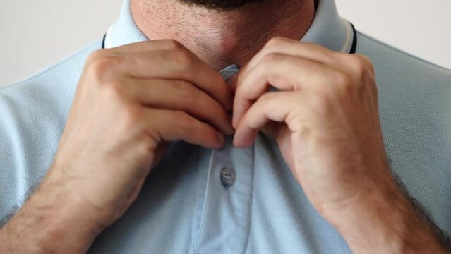 Hands buttoning a polo shirt all the way up. Close up of how to button the collar of a colored polo. Man adjusting his poloshirt. Buttoned up style, uniforms and formal dresses. Feeling uncomfortable.