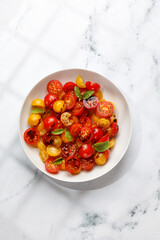Salad with halves of red and yellow tomatoes cherry with basil,  topping balsamic sauce on white plate. Vegetarian and vegan food. Keto diet. Top view.