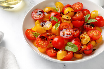 Healthy Salad with cherry red and yellow tomatoes, topping balsamic sauce and basil on white plate. Fresh salad bowl.