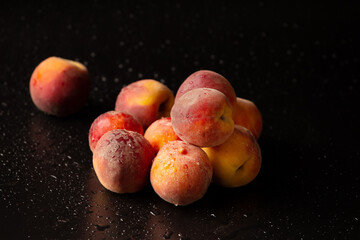 Fresh ripe juicy whole and cut red peaches on rough black background.
