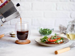 Balanced breakfast of sandwich with cheese, tomatoes, green and pouring hot coffee on light background. Diet food.