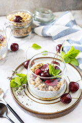 Healthy menu concept. Home made granola breakfast. Glass of parfait made of granola, berries cherry, yogurt with chia seeds on rustic table.