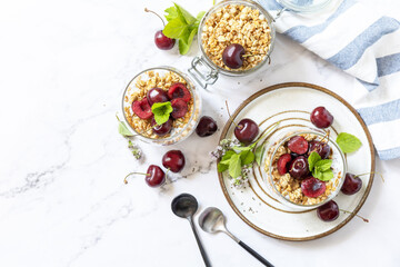 Healthy menu concept. Home made granola breakfast. Glass of parfait made of granola, berries cherry, yogurt with chia seeds on rustic table. View from above. Copy space.