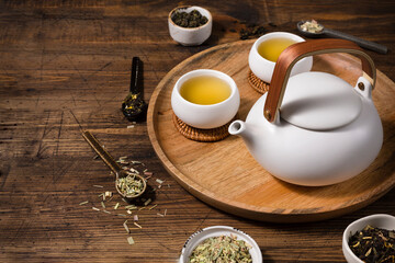A white teapot and two cups of lemongrass tea on a wooden tray. View from above.