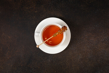 A cup of black tea and caramel sugar on brown background. Top view. Copy space.
