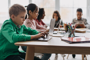 Boy Using Laptop Sitting With Multiethnic Classmates In Modern Classroom