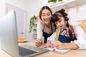 Happy asian mother and daughter having video call, waving and smiling at laptop screen, sitting in kitchen .School girl using computer, having online lesson while coronavirus pandemic.