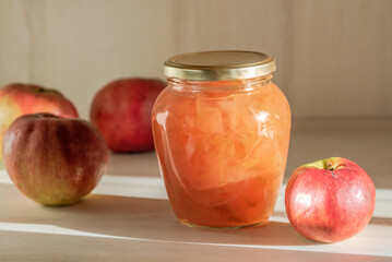 Glass jar with apple jam on the wooden surface among red and yellow apple fruits