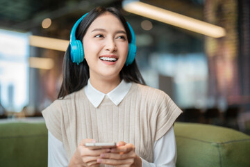 relax joyful casual asian female adult woman casual cloth enjoy listening music from streaming online playing music playlist application on smartphone via earphone  on sofa couch at co working space