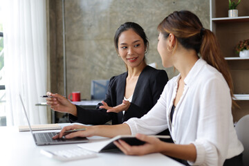 Obraz premium Attractive Asian businesswoman and secretary colleague discussing working on a business project at an office desk.