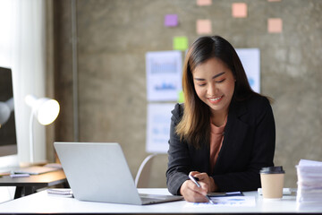 Fototapeta premium Attractive Asian businesswoman working on laptop and reading documents in office.