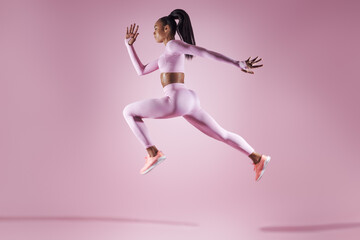 Fototapeta na wymiar Confident young woman in sports clothing jumping against pink background