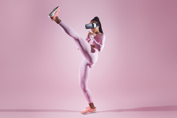 Woman in virtual reality headset practicing in kicking while standing against pink background