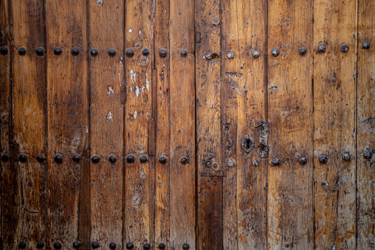 Antique weathered double leaf door with metal knockers and decorations on dark natural wood