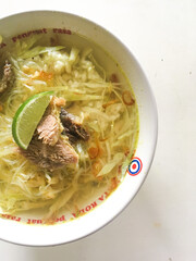 Yogyakarta, Indonesia-August, 2022 : beef soto served with rice noodles and lime isolated on white background
