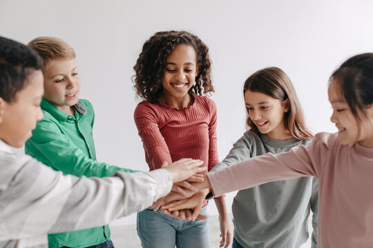 Cheerful Kids Putting Hands Together Standing In Circle Posing Indoors - Powered by Adobe