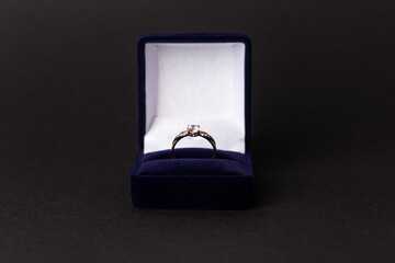 Jewelry, gold diamond ring in a blue box on a black background, isolated.  A ring for a marriage proposal. Close-up. Front view. A place for your text.