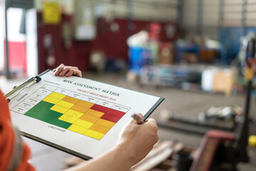 A manager is holding a pen and risk matrix form with factory workshop place as blurred background....