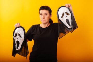 a woman on a yellow background 50 years old holds two masks in her hands on Halloween