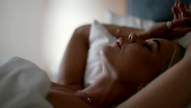 excited woman is lying in bed and enjoying caress during sex, portrait of seductive blonde lady