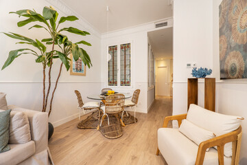 Dining room with wicker chairs and table with wicker foot and glass top, green houseplants, sofa and chestnut hardwood floors