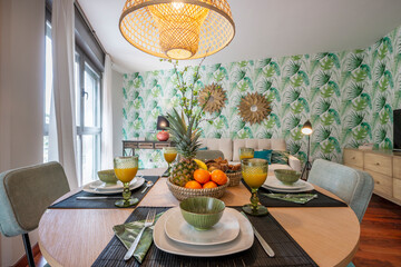 Beautiful round wooden dining table with breakfast service set up with assorted fruits, glasses of juice and a wicker lamp on the ceiling