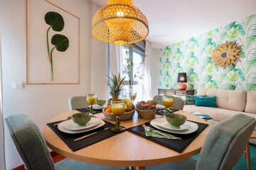 Beautiful round wooden dining table with breakfast service set up with assorted fruits, glasses of juice and a wicker lamp on the ceiling