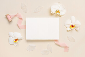 Blank card near white orchid flowers and pink silk ribbons on light beige, Wedding mockup