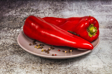 Two red sweet allspice on a plate on a gray background