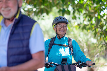 Active senior caucasian couple with electric bicycles outdoors in the park. Two happy elderly people running in nature enjoying healthy lifestyle