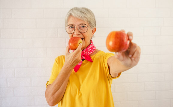 Smiling Senior Woman In Yellow T-shirt On A White Background Holding Two Red Apples Fruit In Her Hands Looking At Camera - Healthy Eating Concept