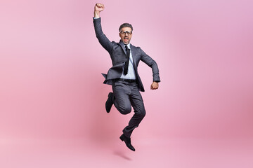Excited mature man in full suit jumping and gesturing against pink background