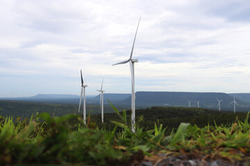 Aerial photo of a nice windmill in green forest and mountain with white clouds in the blue sky. Wind turbines for electric power with clean and Renewable Energy concept.