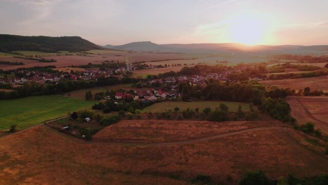 Aer ial view of a German village surrounded by meadows, farmland and forest at sunset in Germany.