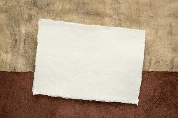 small sheet of blank white Khadi rag paper from South India against abstract landscape in earth tones