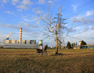 Mężczyzna z rowerem turystycznym przed uschniętym drzewem brzozy, elektrownia.