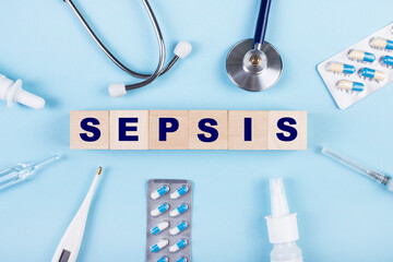 On a blue background, a stethoscope, a thermometer, other medicines and wooden cubes with the text SEPSIS. View from above. Medical concept