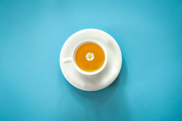 A cup of chamomile tea on blue background, flat lay.