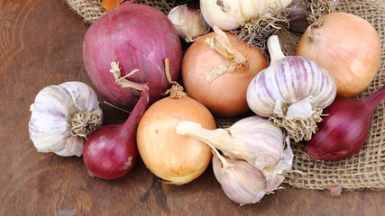 Closeup of different own grown sorts of onion and garlic on a wooden background. Top down view.