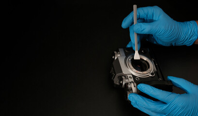 Technician cleans sensor of digital camera from dust and dirt using cleansing swab, Tools for cleaning on a dark textured background.
