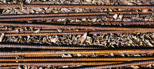 Top view old rusted iron bars and dry leaves on floor. Close up to stack of straight old rusty steel reinforcement structural steel bars from construction site. Steel rod with rust. Rusty Metal Bars.