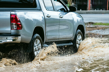 Pickup truck passing through flooded road. Driving car on flooded road during flood caused by torrential rains. Flooded city road with large puddle. Splash by car through flood water. Selective focus. © JinnaritT