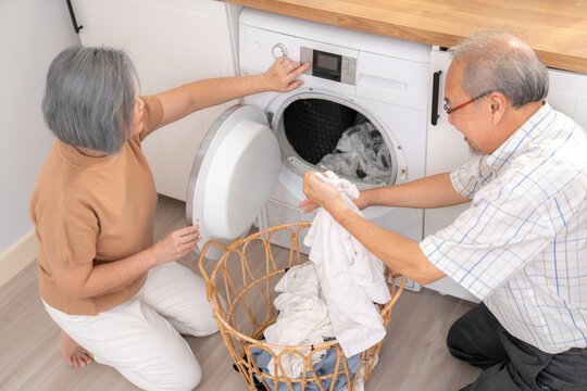 Senior couple working together to complete their household chores at the washing machine in a happy and contented manner. Husband and wife doing the usual tasks in the house.
