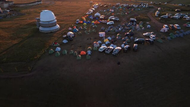 Bright dawn over the Assy-Turgen Observatory in the mountains. Aerial view from the drone of the camp of tents, cars and waking tourists. There is an old abandoned building. Kazakhstan, Almaty