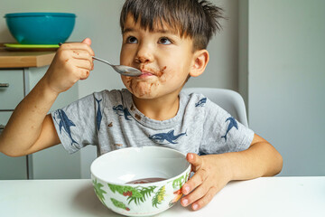 Little boy with chocolate on face eats his pudding very enjoyable